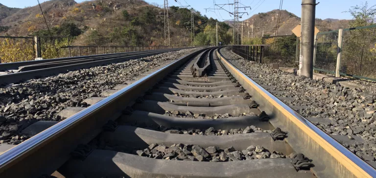 Eisenbahnstrecke biegt rechts ab, Schotterbett, Oberleitung, Bäume und Berge.